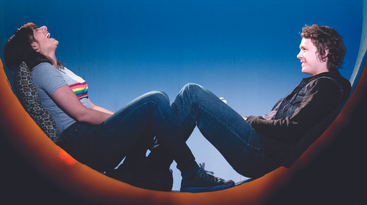 A man and a woman sit within a circle against a blue backdrop