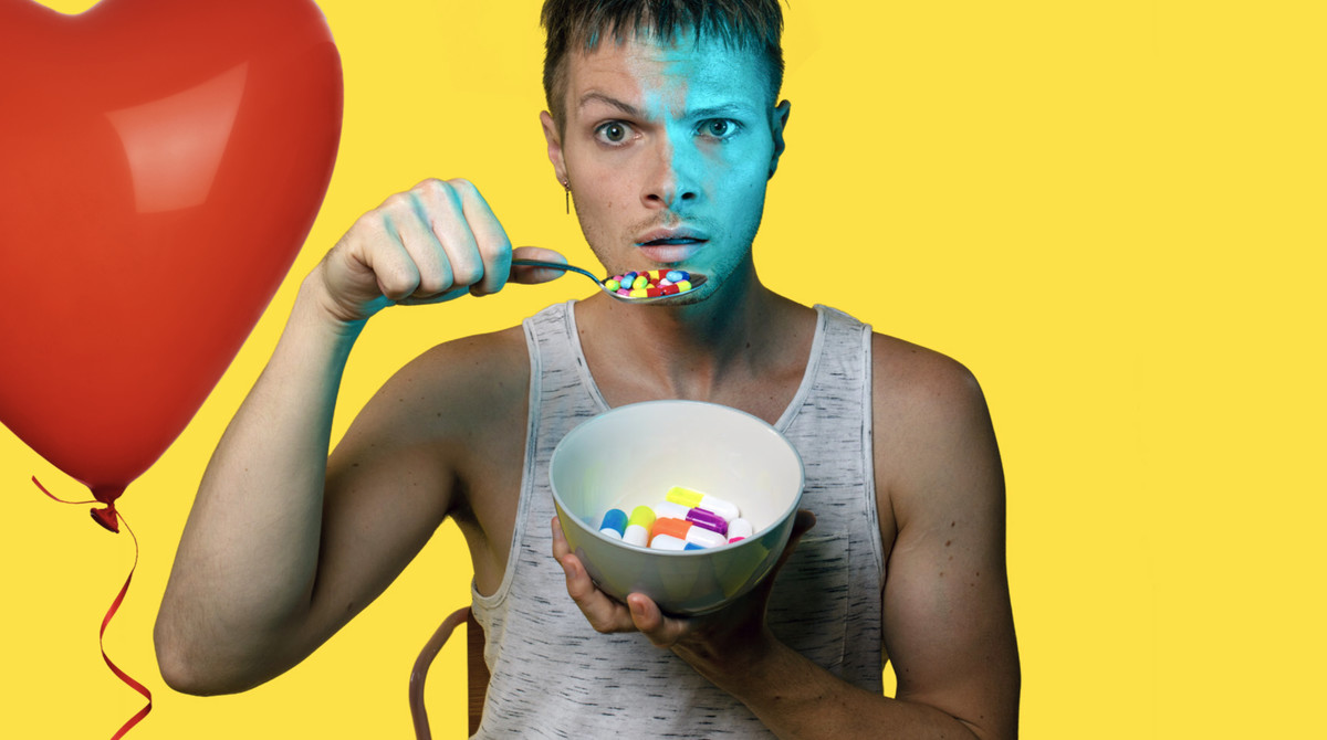 Nathaniel Hall, a white young man, stands against a yellow background, wearing a grey vest top and scoops a bowl of pills from a cereal bowl. A red heart-shaped balloon floats behind him.